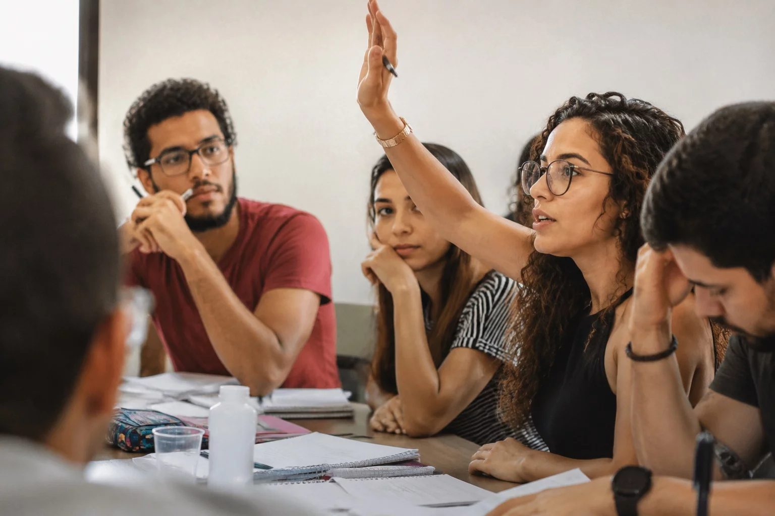 Estudante levantando a mão em uma mesa de seminário coberta de anotações