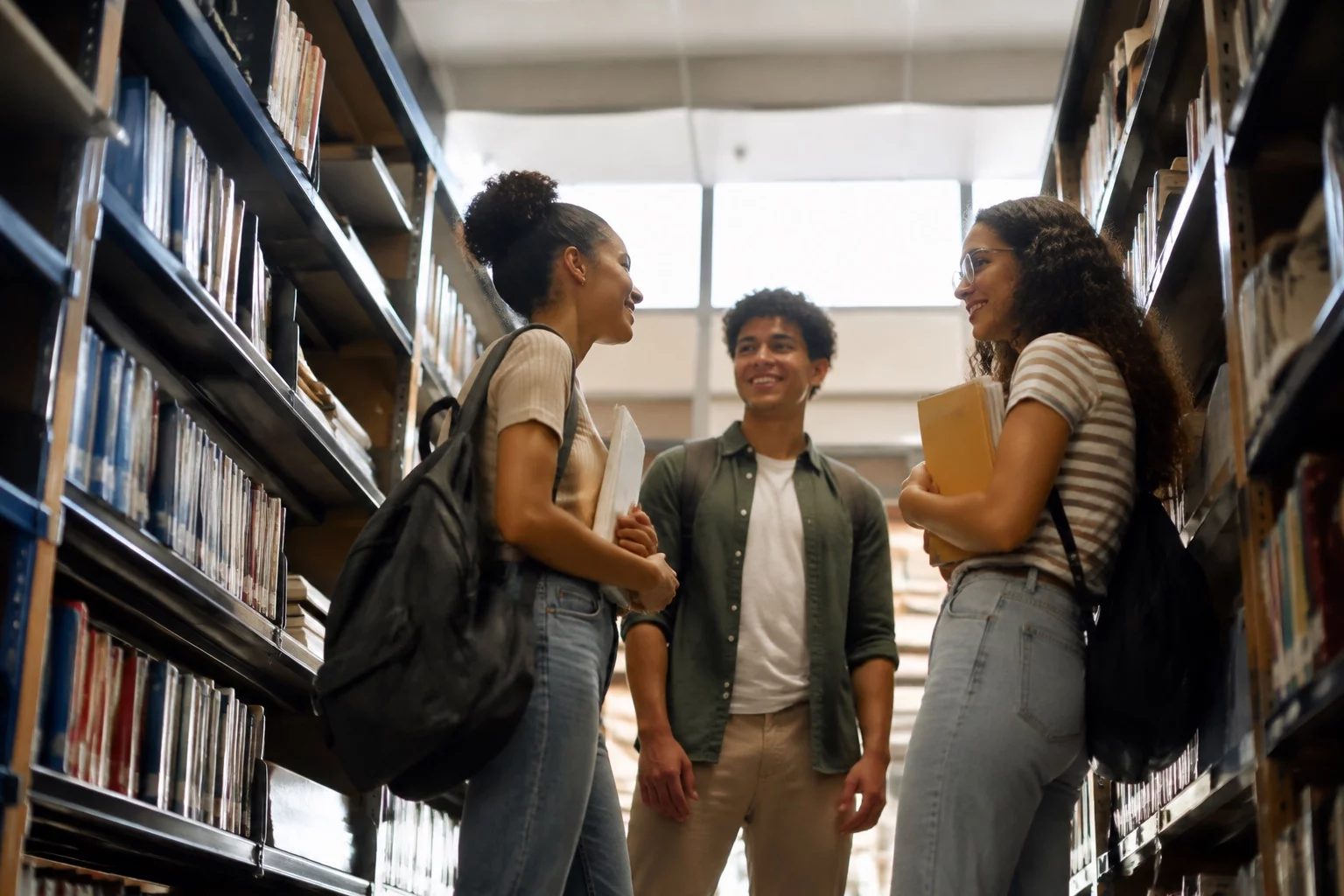 Estudantes conversando em pé entre as estantes de uma biblioteca